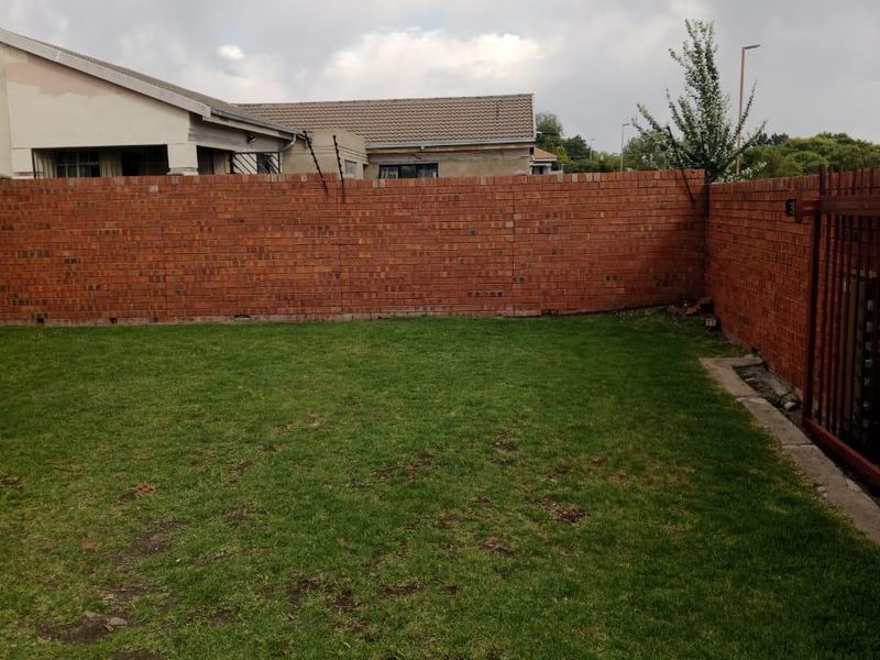 A private backyard featuring a lawn enclosed by a brick perimeter wall with integrated electric fencing and a metal gate.