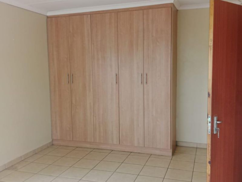 A clean, empty bedroom featuring neutral tiled flooring and a large, light-wood built-in wardrobe with ample storage space.