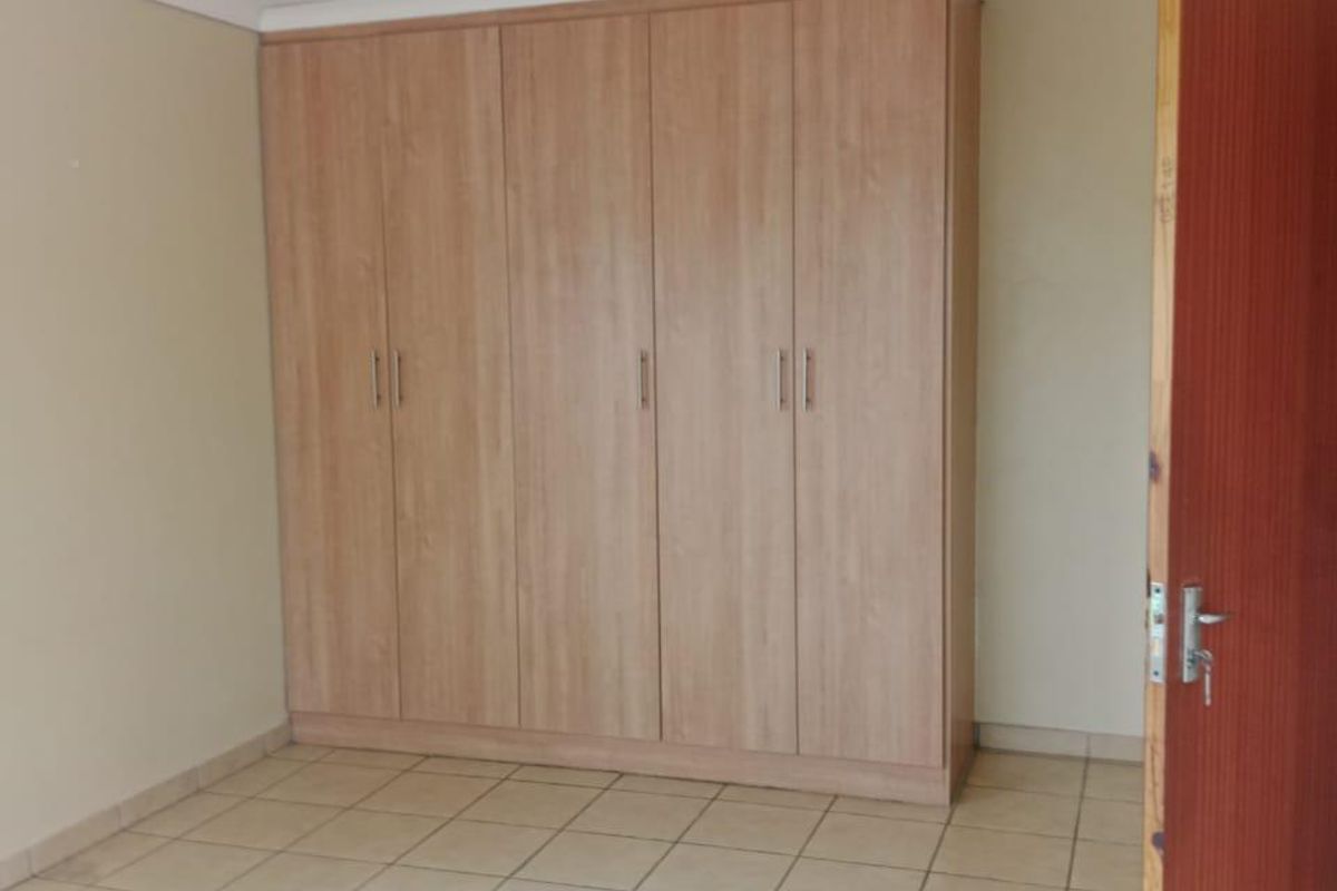 A clean, empty bedroom featuring neutral tiled flooring and a large, light-wood built-in wardrobe with ample storage space.