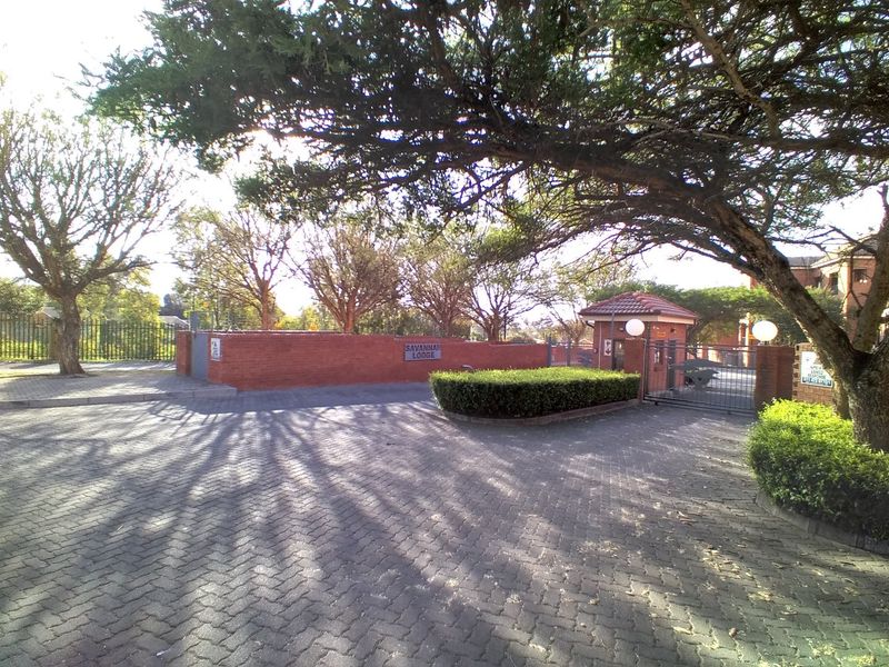 The entrance to Savannah Lodge featuring a paved driveway, brick boundary wall, and a secure guard house.