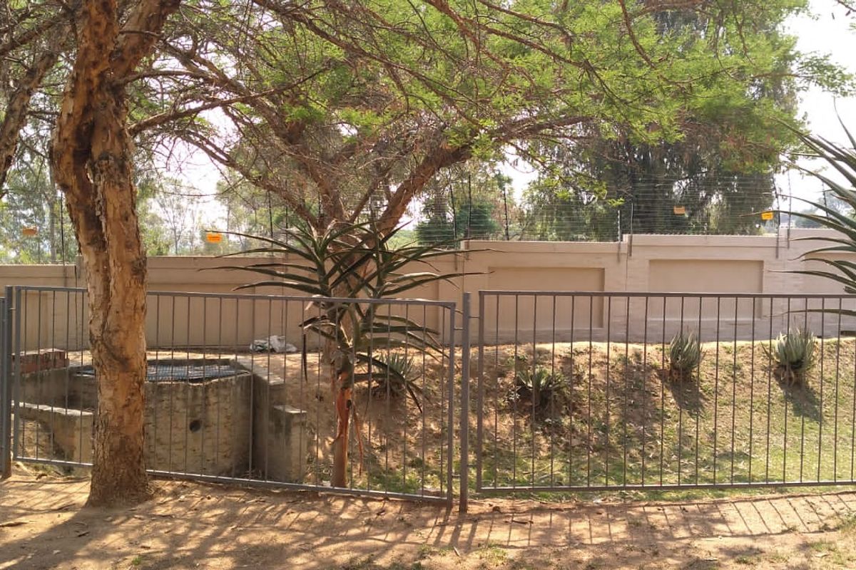 Rear exterior area featuring a perimeter wall with electric fencing, metal security fencing, and established trees and landscaping.
