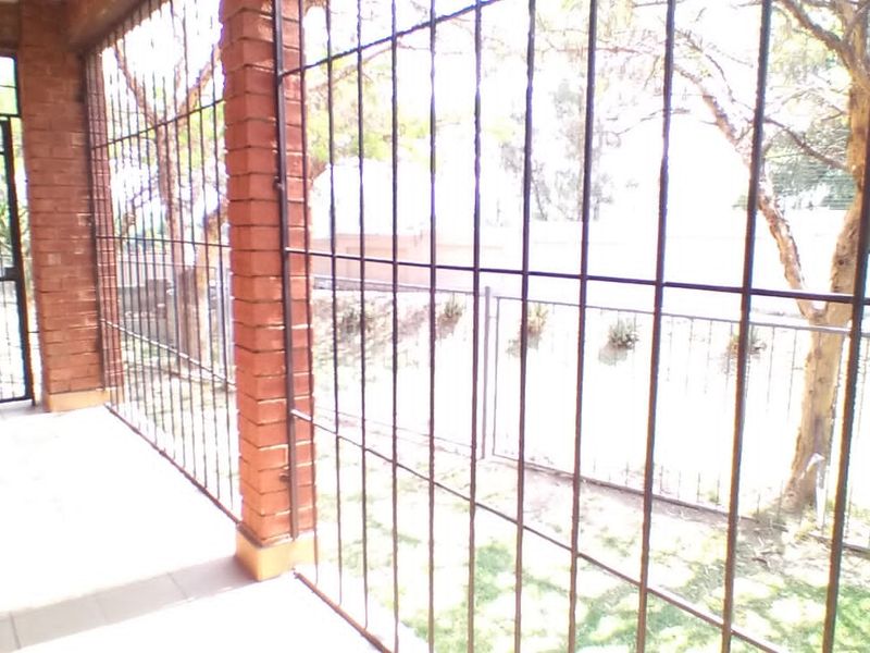 A covered patio area featuring brick pillars and security bars, providing a secure outdoor space with tiled flooring.