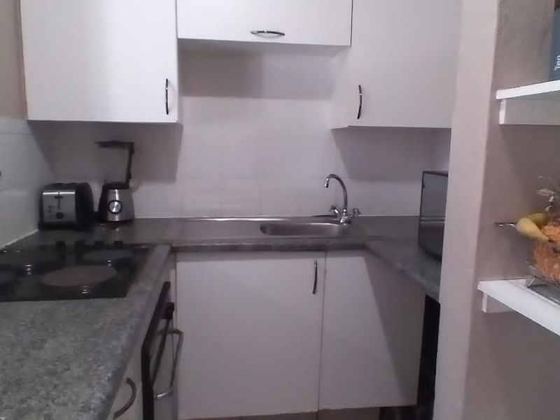 Compact kitchen featuring white cabinetry, dark laminate countertops, an integrated electric hob, and a stainless steel sink with tiled splashback.