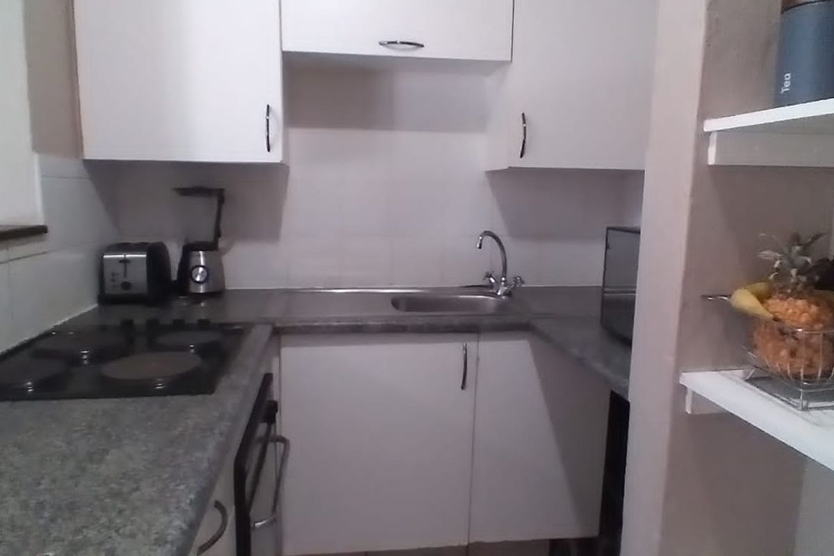 Compact kitchen featuring white cabinetry, dark laminate countertops, an integrated electric hob, and a stainless steel sink with tiled splashback.
