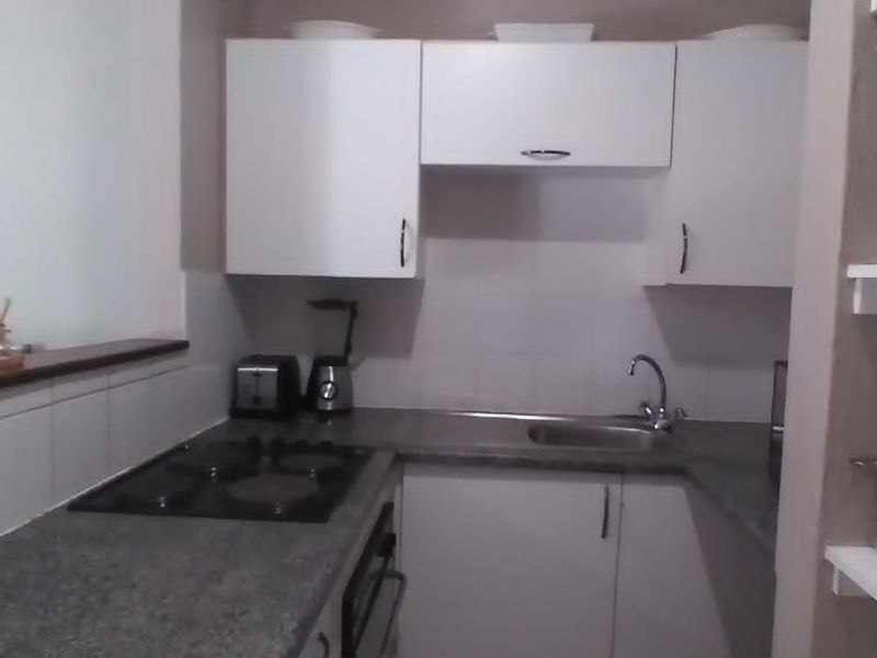 Compact kitchen featuring white cabinetry, laminate countertops, a built-in hob, and a stainless steel sink with tiled splashback.