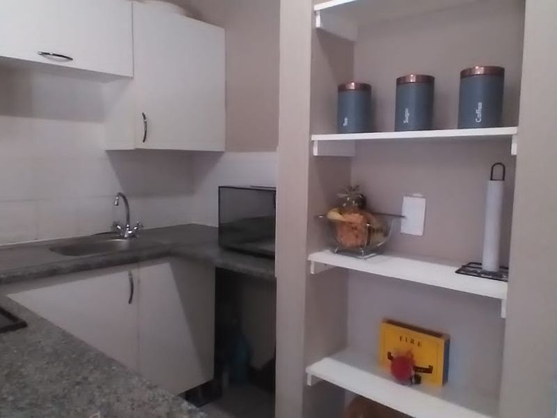 A compact kitchen featuring white cabinetry, granite-look laminate countertops, a built-in electric hob, and integrated open shelving for storage.