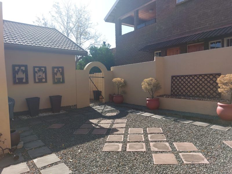 A private courtyard garden featuring paved stepping stones, gravel landscaping, a decorative arched gate, and perimeter boundary walls.