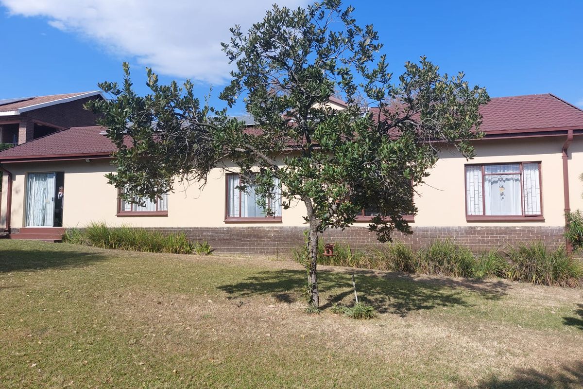 A view of the rear exterior of the house featuring a brick and plaster facade, tiled roof, and a spacious lawn with a mature tree.