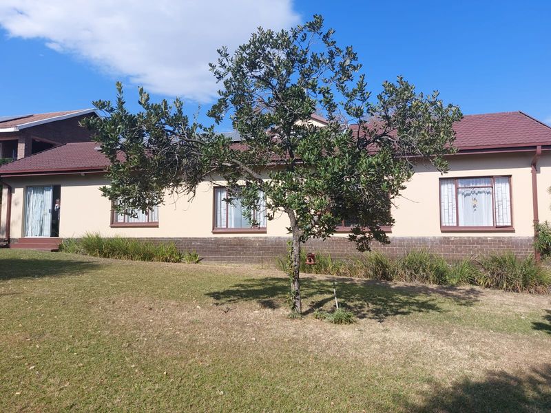 A view of the rear exterior of the house featuring a brick and plaster facade, tiled roof, and a spacious lawn with a mature tree.