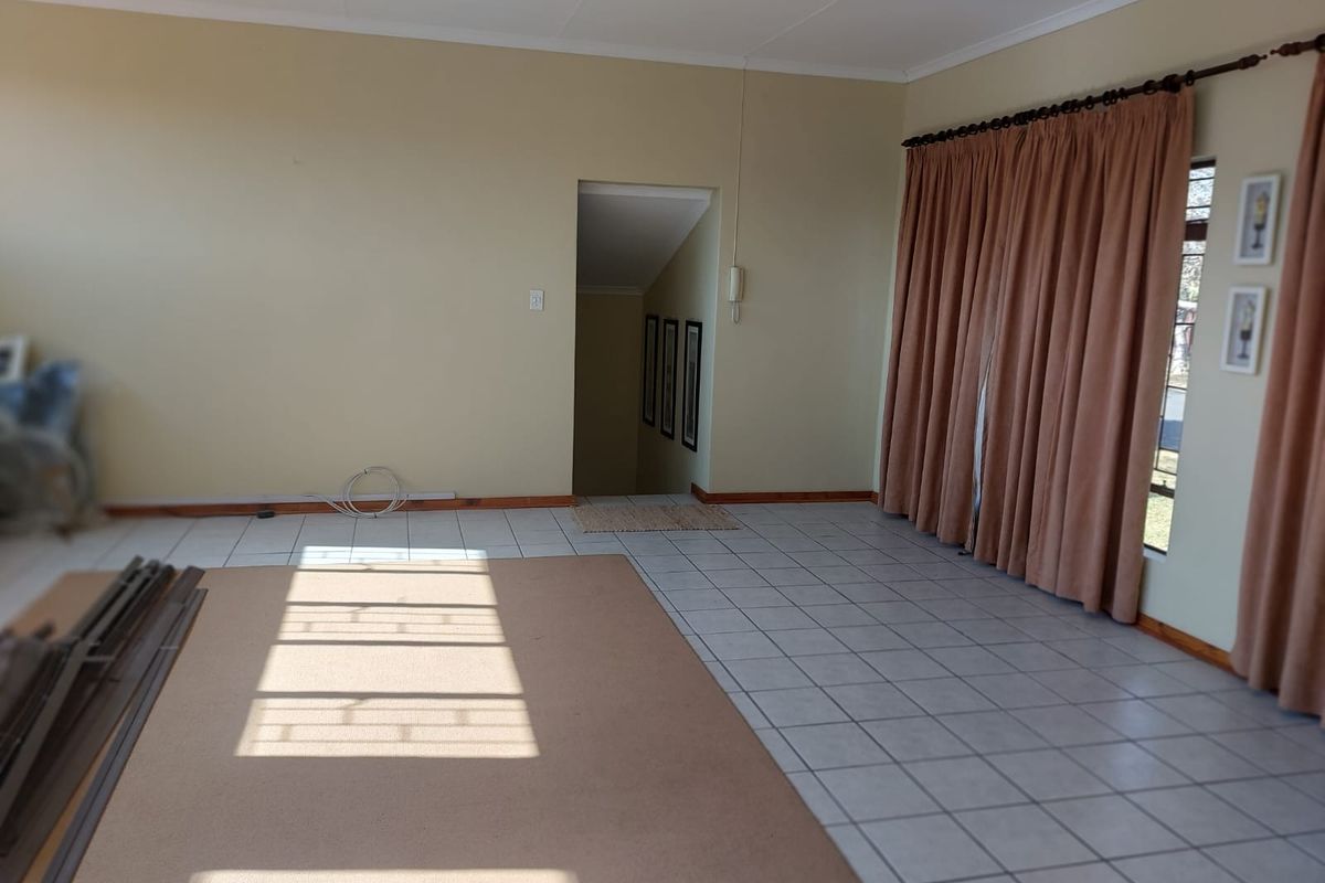 Spacious living area featuring neutral tiled flooring, large windows with curtains, and direct access to a staircase.