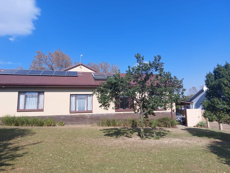 Front exterior view of a single-story house featuring a tiled roof, solar panels, solar geyser, and a well-maintained lawn.