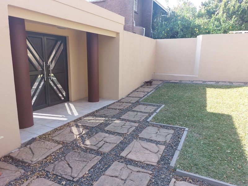 A private rear courtyard featuring a paved walkway, manicured lawn, and a covered entrance with decorative double doors and structural columns.