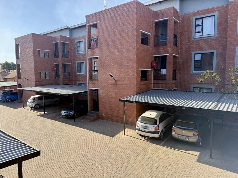 Exterior view of a multi-story face brick apartment complex featuring covered parking bays and paved driveway access.