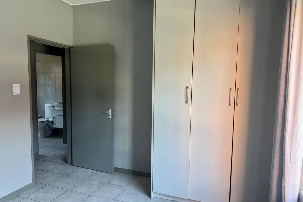 A bedroom featuring tiled flooring and built-in cupboards, with an adjacent view into a bathroom.