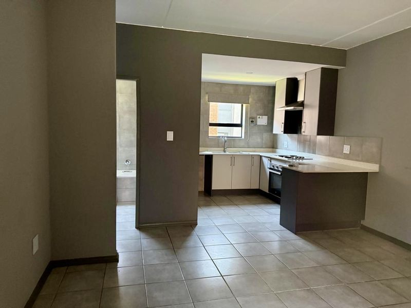 Open plan kitchen featuring modern cabinetry, stone countertops, and built-in appliances, seamlessly connected to the living area with tiled flooring throughout.
