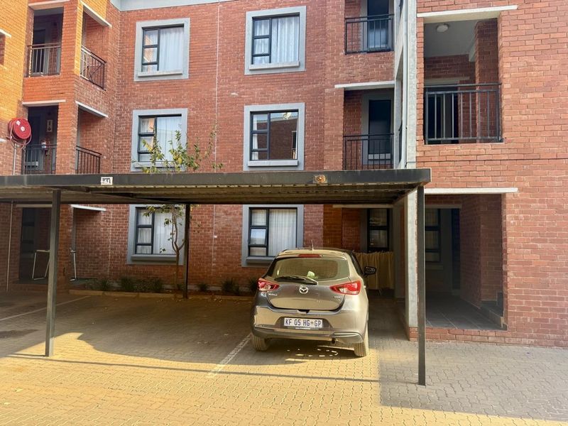 Exterior view of a multi-story face brick apartment building featuring covered parking bays and private balconies.