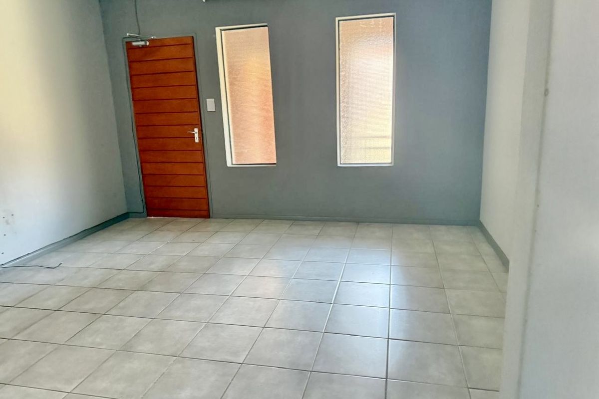 An empty living room featuring neutral tiled flooring, a timber door, and two vertical windows with grey painted walls.