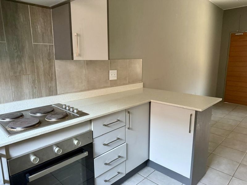 A clean, modern kitchen featuring built-in cabinetry, stone countertops, and a fitted electric hob and oven with neutral tiled finishes.