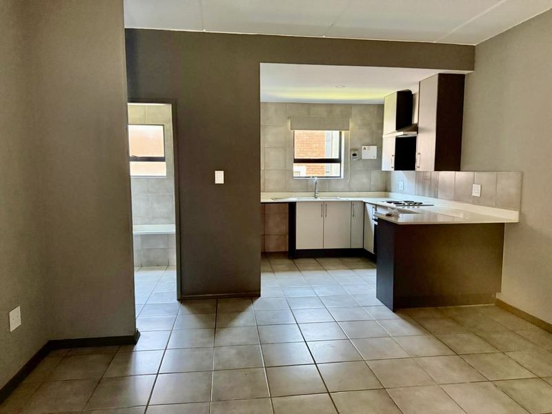 Open plan kitchen area featuring tiled flooring, modern cabinetry, stone countertops, and a built-in hob, with an adjacent utility or scullery space.