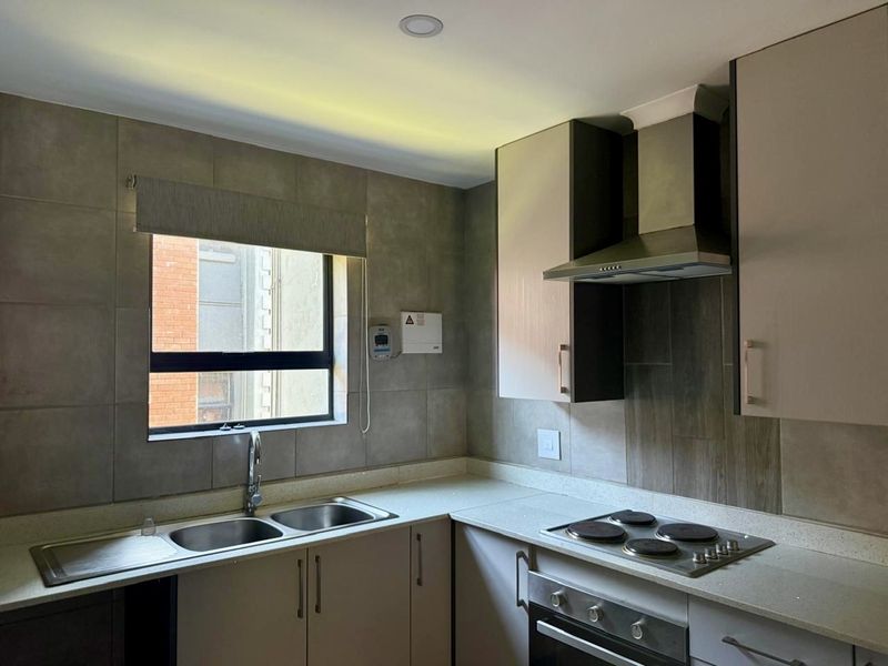 Modern kitchen featuring built-in cabinetry, stone countertops, a double sink, and integrated appliances including an electric hob, oven, and extractor fan.