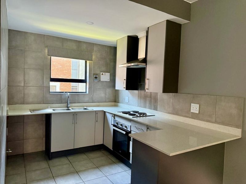 A modern, well-maintained kitchen featuring stone countertops, built-in cabinetry, an electric hob, oven, and extractor fan with neutral tiled finishes.