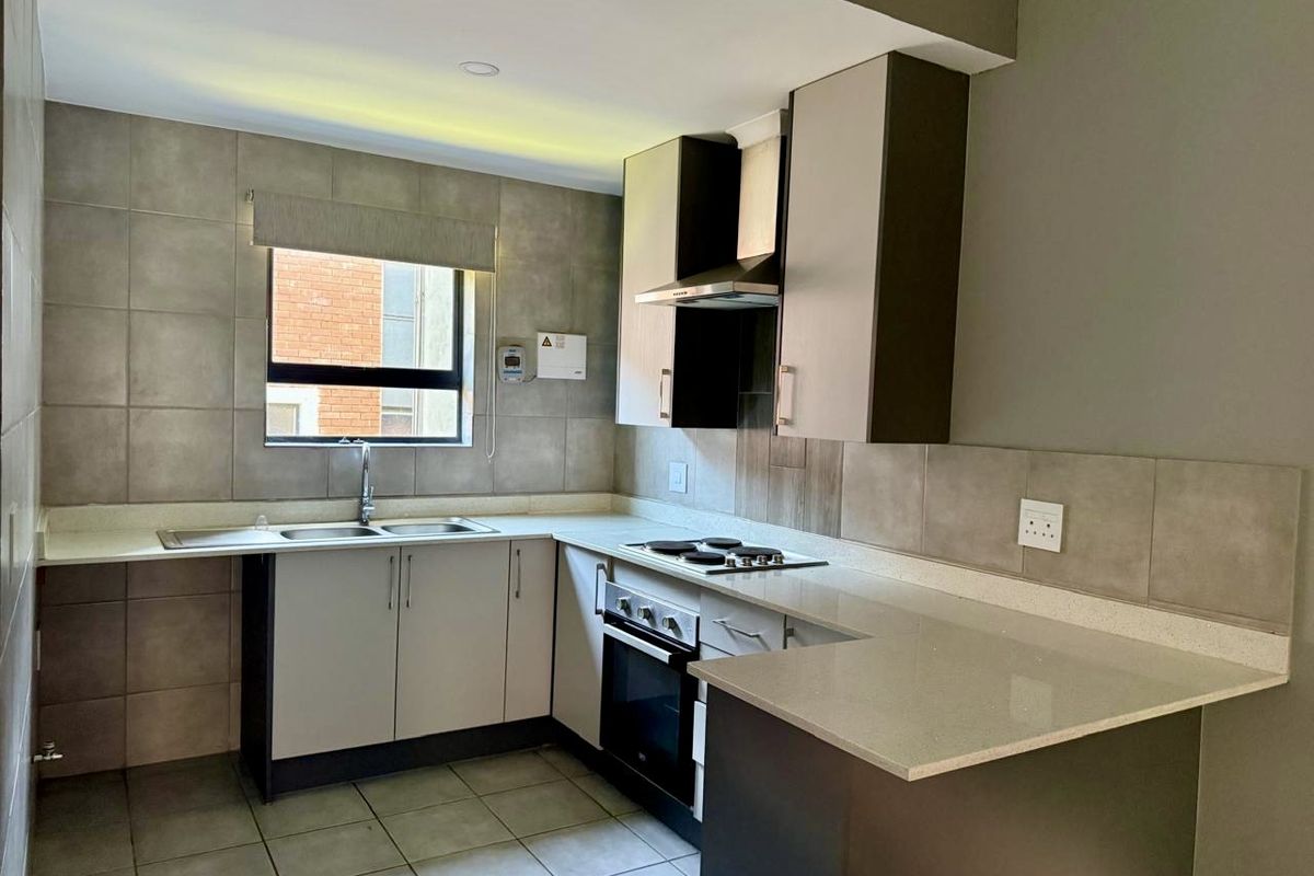 A modern, well-maintained kitchen featuring stone countertops, built-in cabinetry, an electric hob, oven, and extractor fan with neutral tiled finishes.