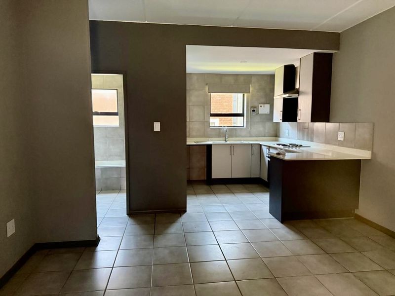 An open-plan kitchen area featuring built-in cabinetry, stone countertops, a hob, and tiled flooring, presented in a clean, vacant state.
