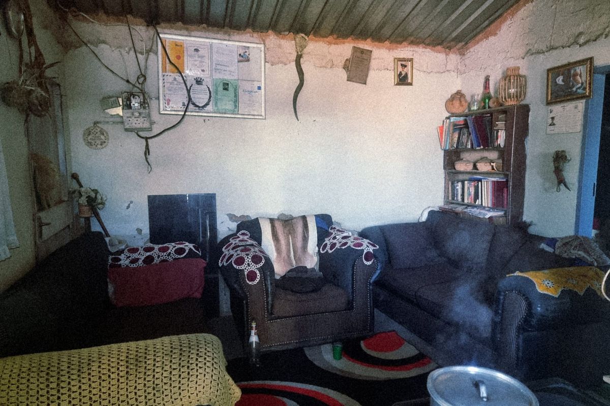 A living room space featuring exposed masonry walls and a corrugated metal ceiling, requiring significant renovation and structural finishing.