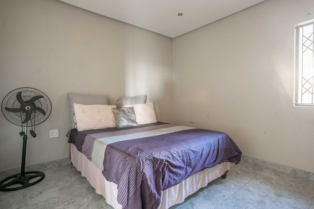 A simple bedroom featuring neutral wall tones, tiled flooring, and a window with security bars.