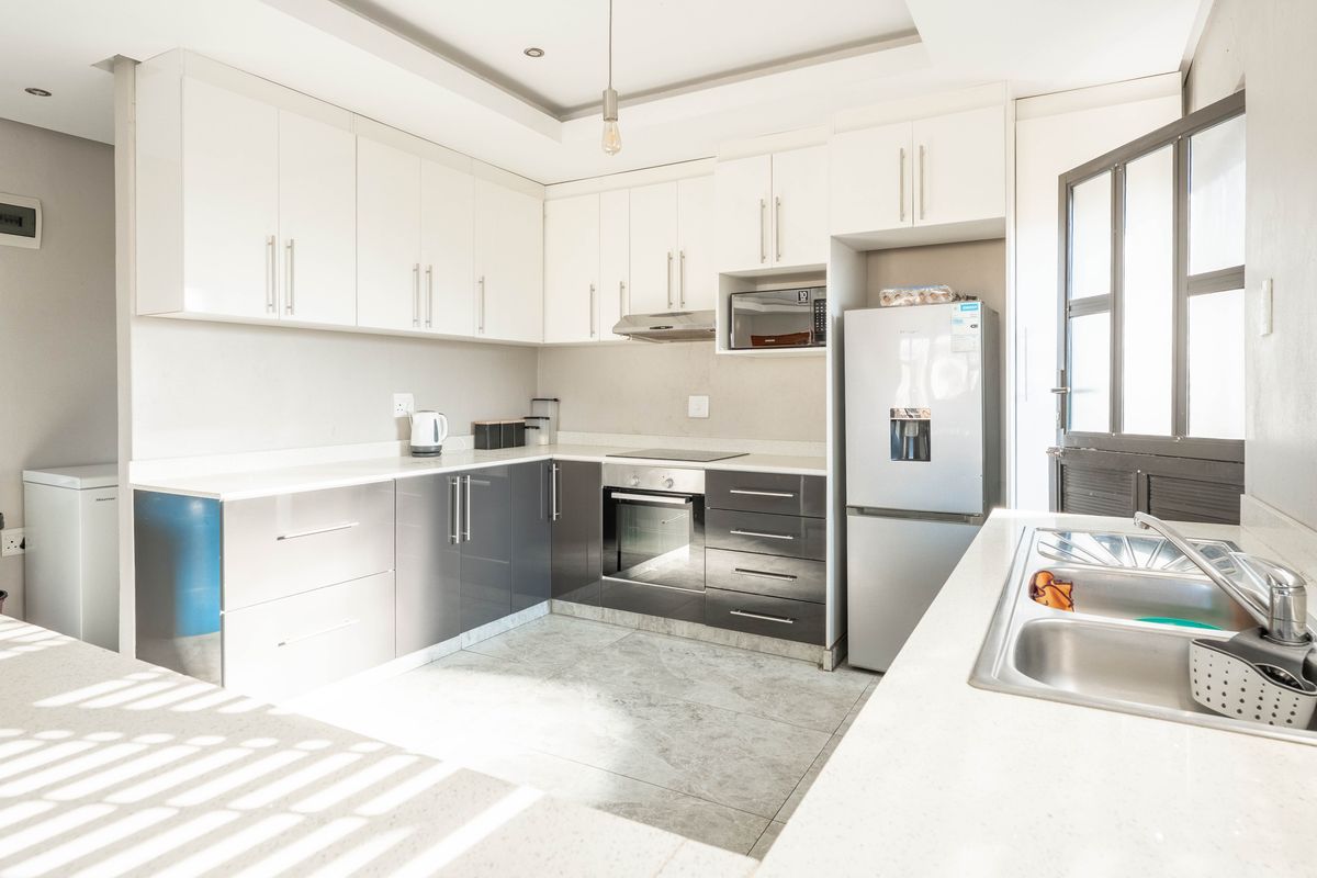 Modern kitchen featuring two-tone cabinetry, stone countertops, integrated oven, hob, extractor fan, and a double stainless steel sink.