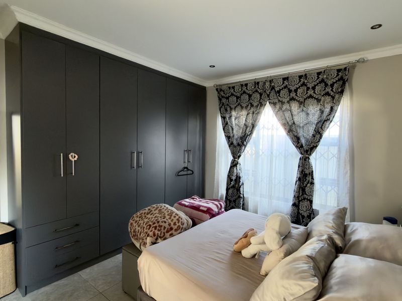 A well-maintained bedroom featuring extensive dark grey built-in cupboards, recessed ceiling lighting, and decorative coving.
