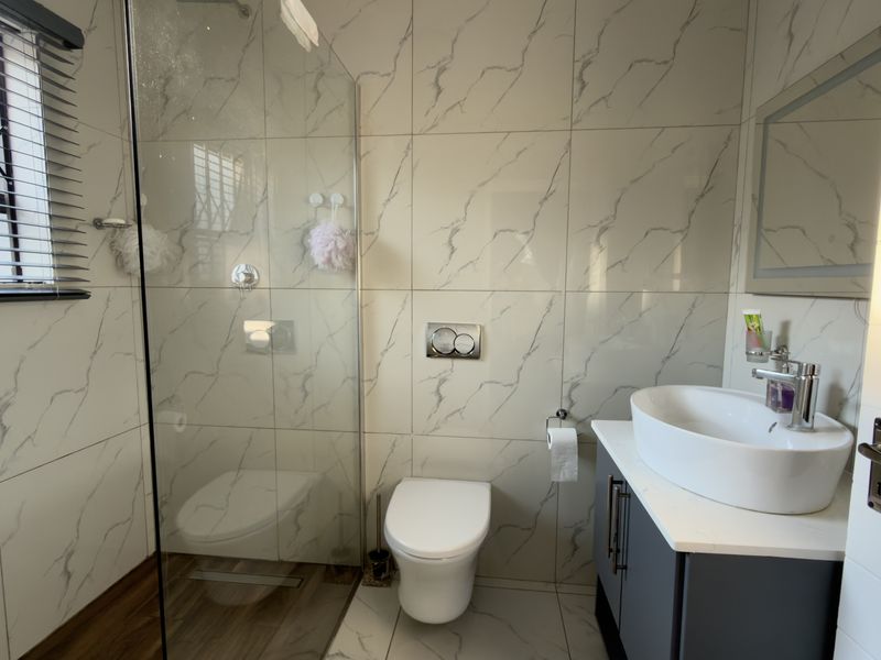 Modern bathroom featuring marble-look wall tiles, a walk-in glass shower, wall-mounted toilet, and a sleek vanity with a countertop basin.