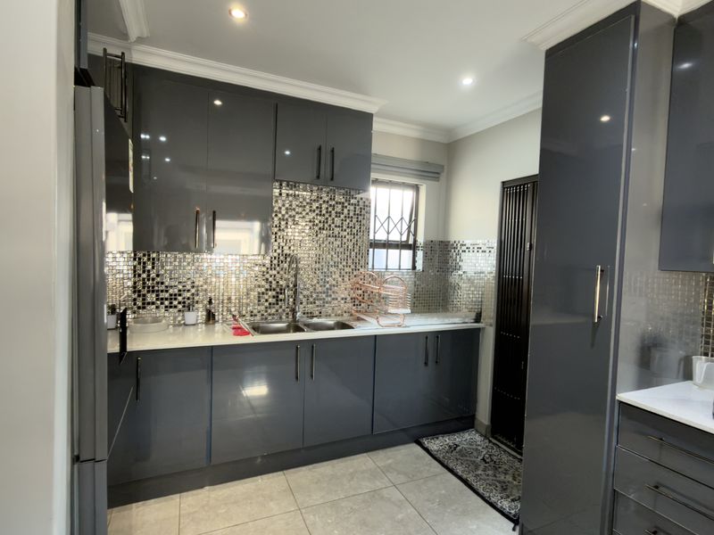 Modern kitchen featuring high-gloss grey cabinetry, stone countertops, and a decorative mosaic tile backsplash with integrated sink and recessed lighting.