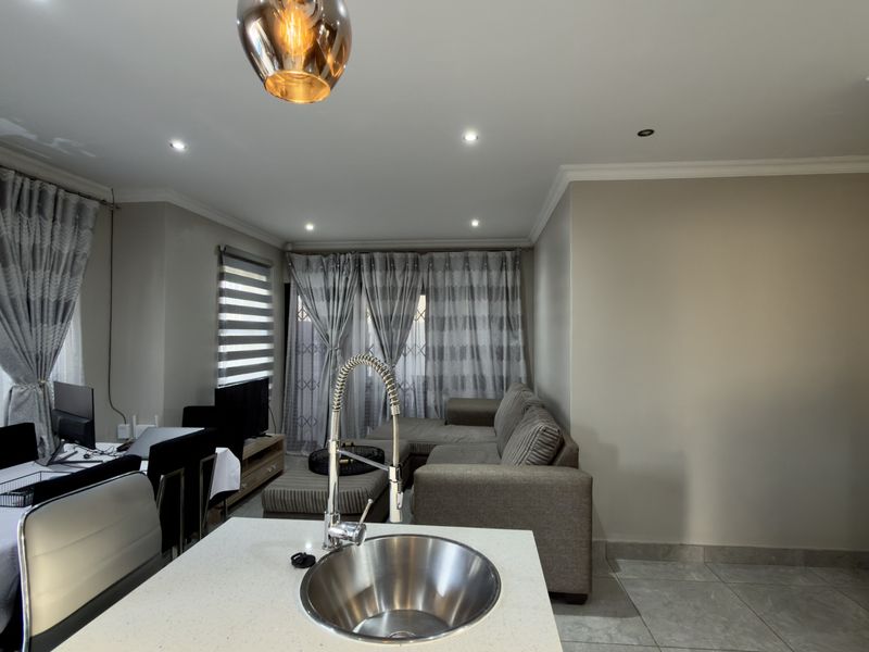 Open-plan living area featuring a kitchen island with a modern sink, recessed lighting, and tiled flooring, seamlessly connecting to the lounge and dining space.