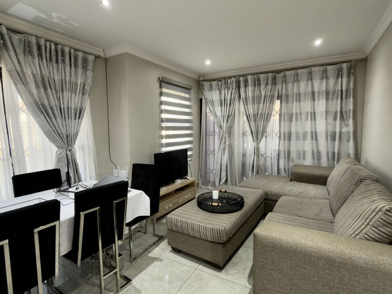 A well-maintained living and dining area featuring neutral tiled flooring, recessed lighting, and large sliding glass doors with integrated window treatments.