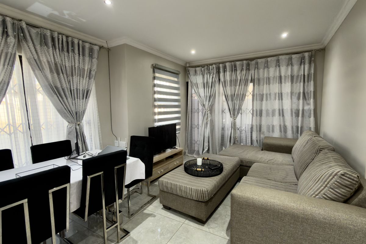 A well-maintained living and dining area featuring neutral tiled flooring, recessed lighting, and large sliding glass doors with integrated window treatments.