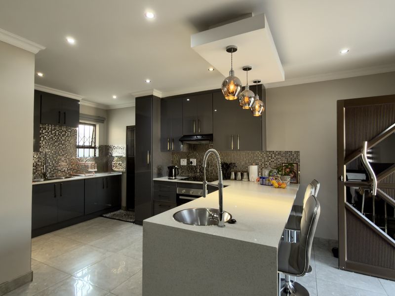 Modern kitchen featuring high-gloss cabinetry, quartz countertops, a central island with a prep sink, mosaic backsplash, and contemporary pendant lighting.