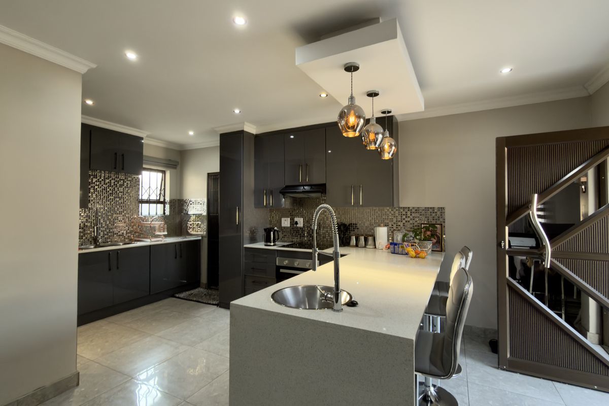 Modern kitchen featuring high-gloss cabinetry, quartz countertops, a central island with a prep sink, mosaic backsplash, and contemporary pendant lighting.