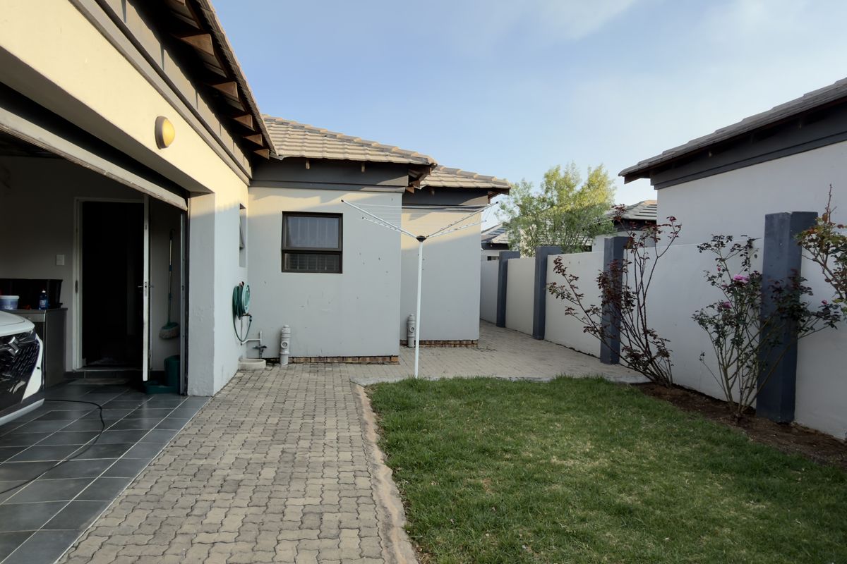 A rear exterior view of the property featuring a paved courtyard, small lawn, boundary walls, and access to the garage area.