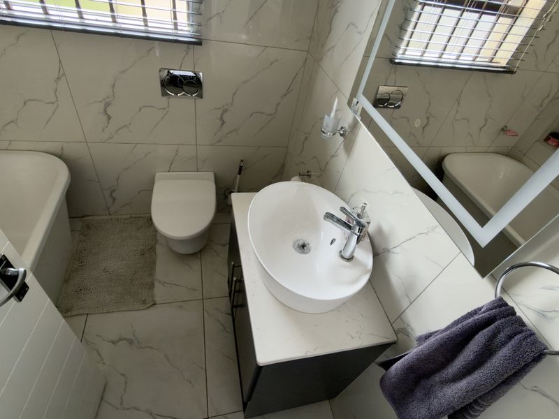 Modern bathroom featuring marble-look wall and floor tiles, a wall-mounted toilet with concealed cistern, a vessel sink vanity, and a bathtub.