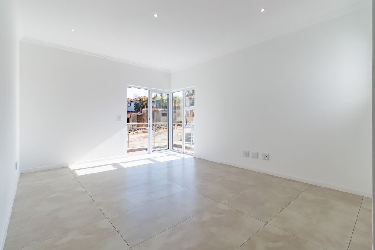 A bright, empty living room featuring large format floor tiles, recessed downlighting, and sliding glass doors leading to an outdoor area.