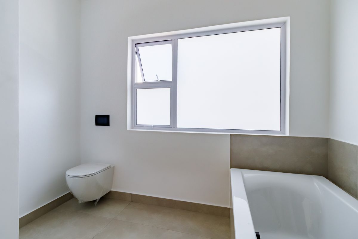 A clean, modern bathroom featuring a wall-hung toilet, a built-in bathtub, and neutral floor tiling with a matching splashback.
