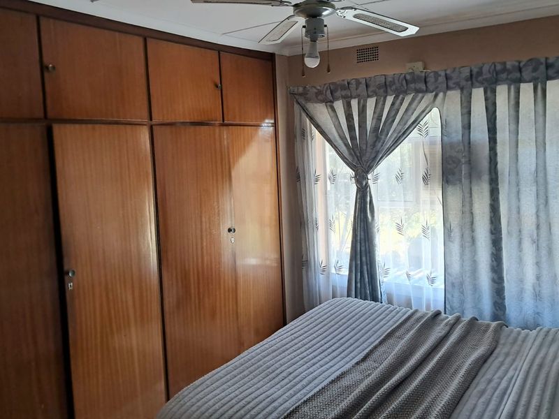 A bedroom featuring floor-to-ceiling built-in wooden cupboards, a ceiling fan, and a window with natural light.