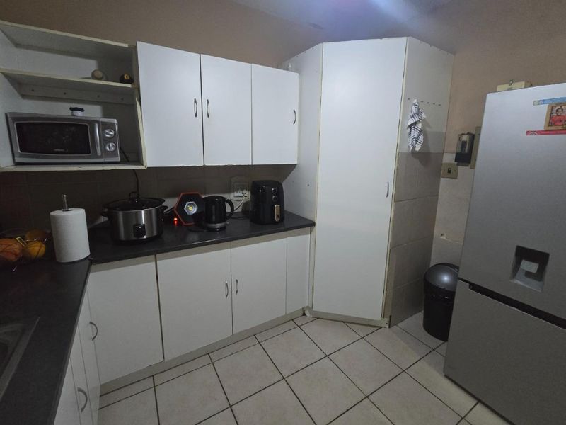 A compact kitchen featuring white built-in cabinetry, dark laminate countertops, and tiled flooring, requiring some cosmetic updates to improve its overall condition.