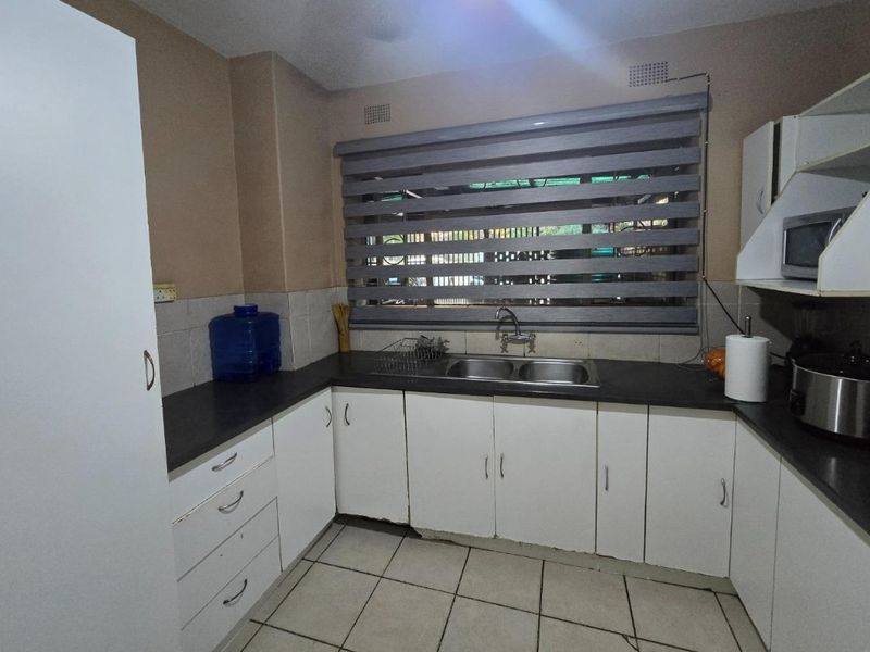 Functional kitchen featuring white cabinetry, dark laminate countertops, double basin sink, and tiled flooring with a window providing natural light.