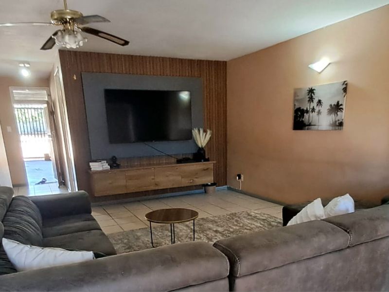 A living room featuring tiled flooring, a ceiling fan, and a modern wall-mounted media unit with decorative wood-look paneling.