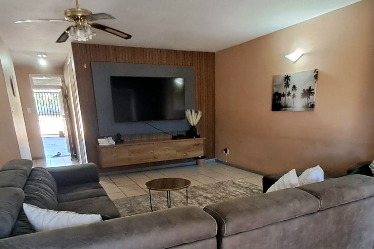 A living room featuring tiled flooring, a ceiling fan, and a modern wall-mounted media unit with decorative wood-look paneling.