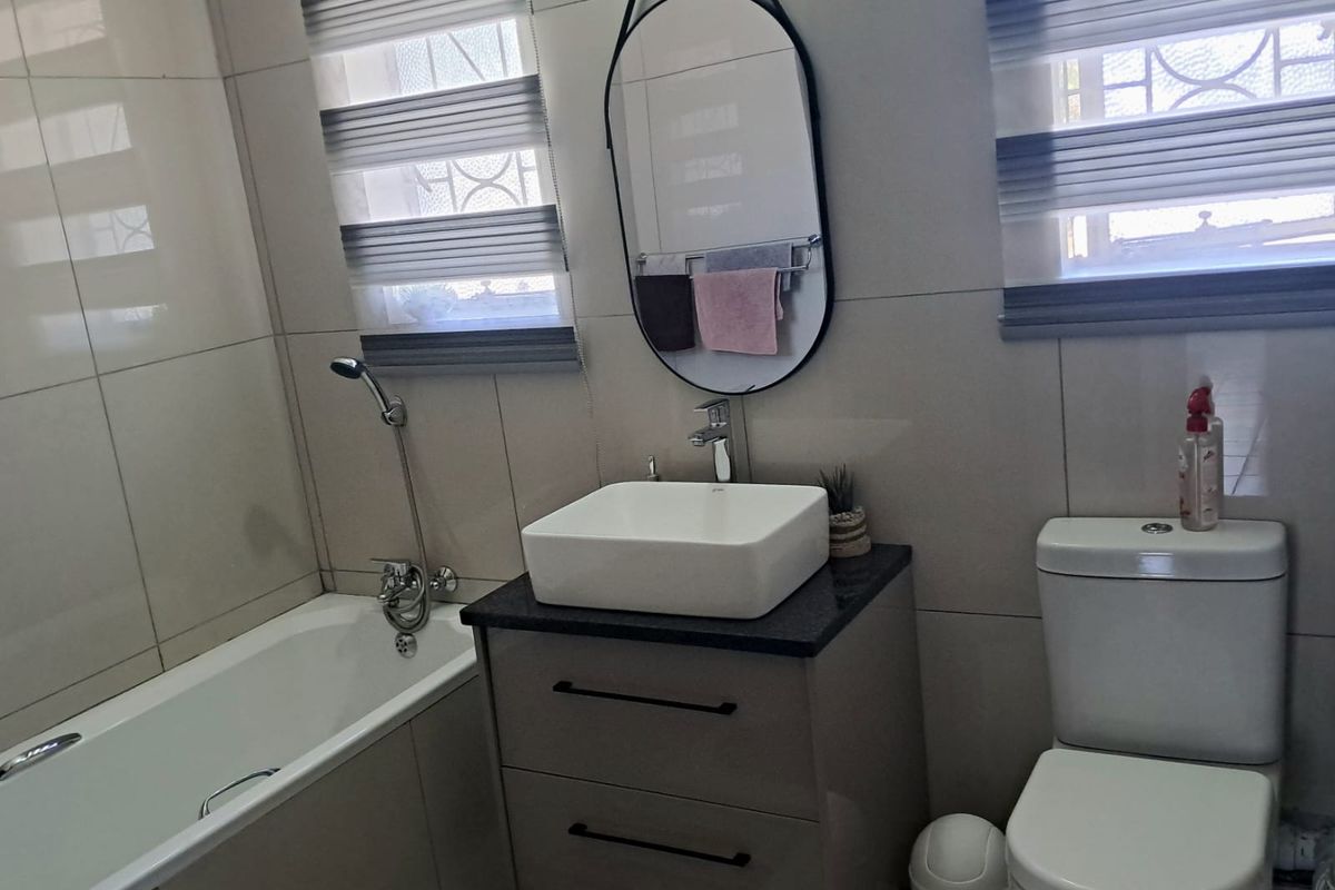 A modern bathroom featuring a bathtub, a vanity cabinet with a vessel sink, and a toilet, finished with neutral wall and floor tiles.