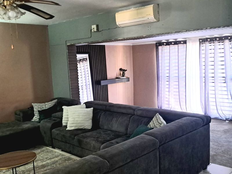 Living room featuring a ceiling fan, wall-mounted air conditioning unit, and decorative slatted wall paneling with a floating shelf.