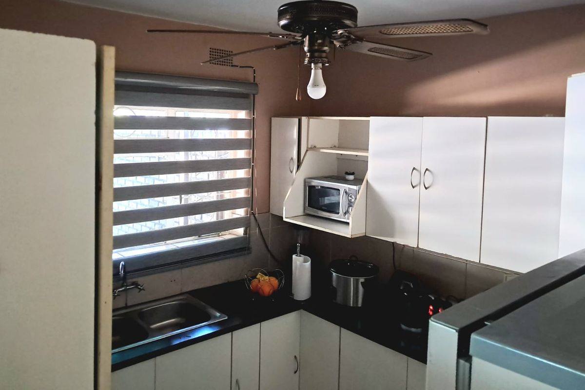 Compact kitchen featuring white built-in cabinetry, dark laminate countertops, a double basin sink, and a ceiling fan with integrated lighting.